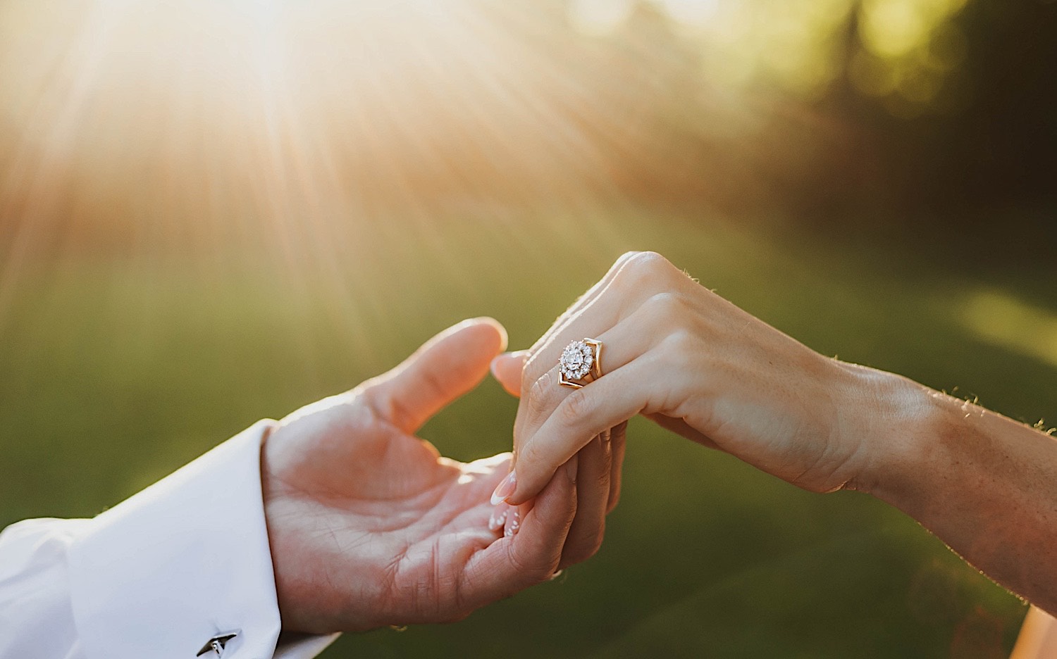 Close up photo of a woman's hand with a wedding ring resting on a man's hand while the sun sets in the background