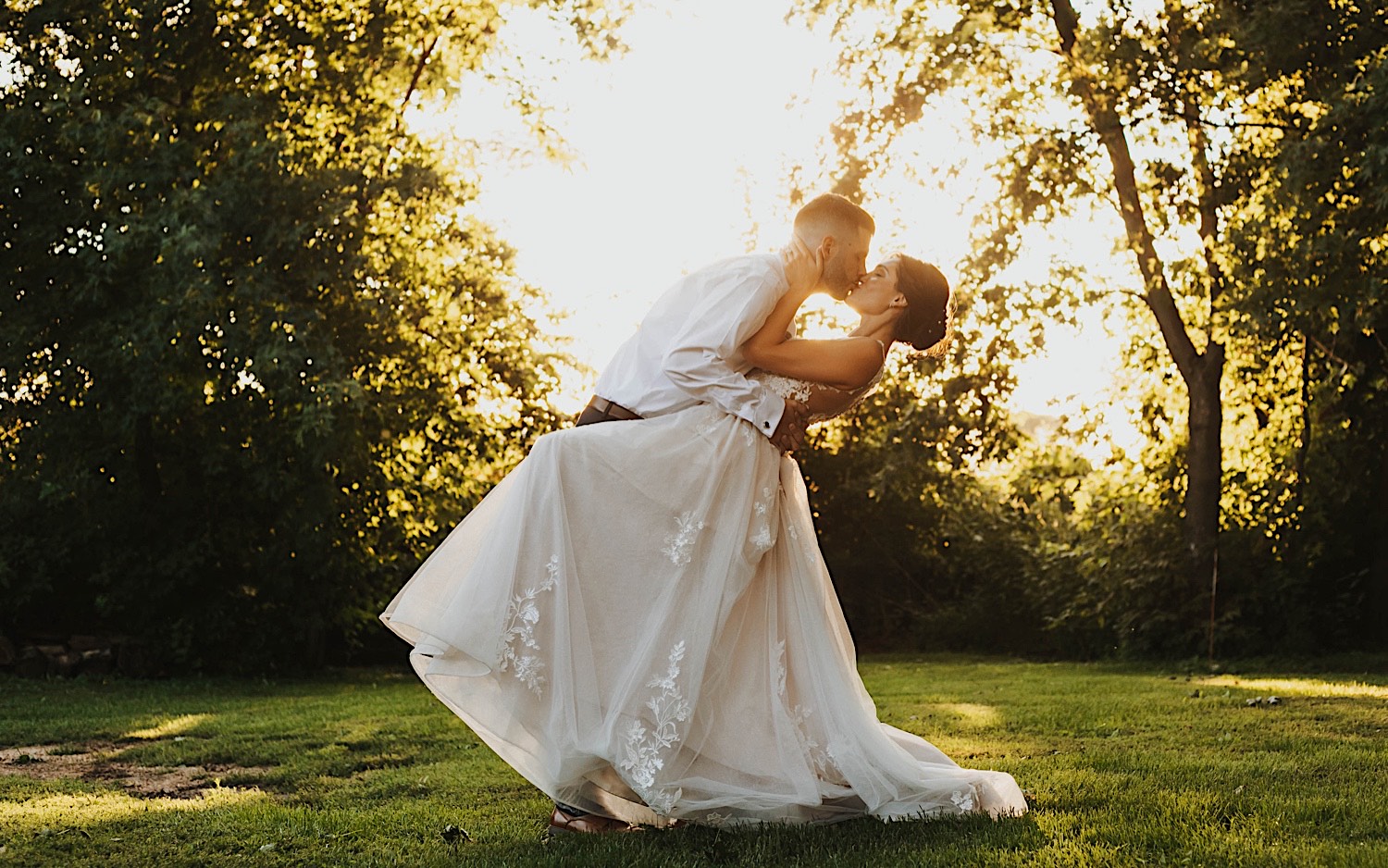 A bride and groom stand outside and kiss one another while the sun sets behind them at their wedding venue Legacy Hill Farm