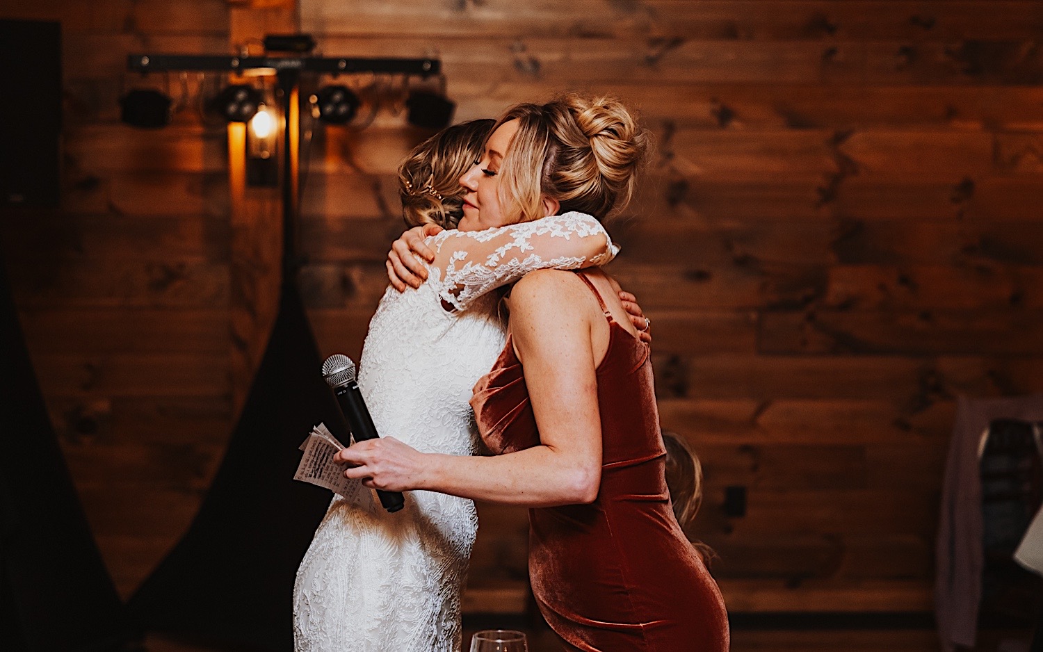 During an indoor wedding reception at Lake Bomoseen Lodge in Vermont, a bride hugs one of her bridesmaids following a speech from the bridesmaid
