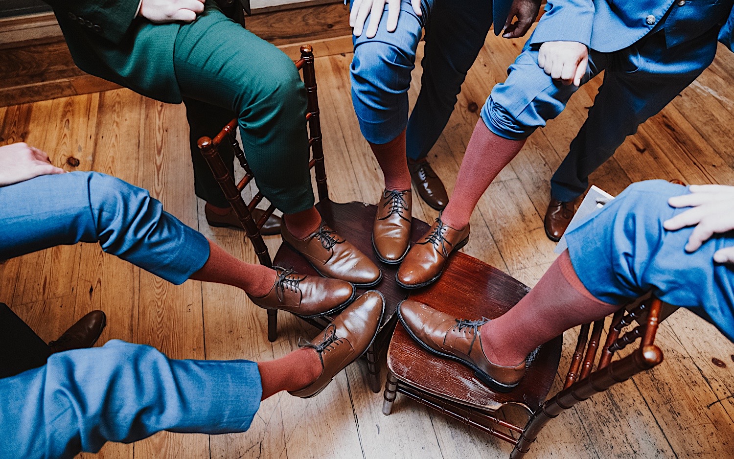 A groom and his groomsmen all put their feet up on a wooden chair to show off their matching shoes during an indoor wedding reception at Lake Bomoseen Lodge in Vermont