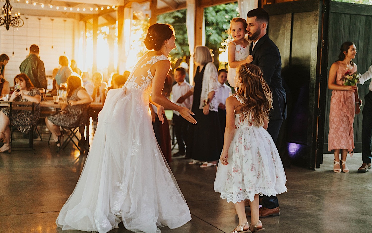 A bride and groom dance with two of their flower girls during their wedding reception at Legacy Hill Farm as the sun sets behind them A bride and groom dance with two of their flower girls during their wedding reception at Legacy Hill Farm as the sun sets behind them