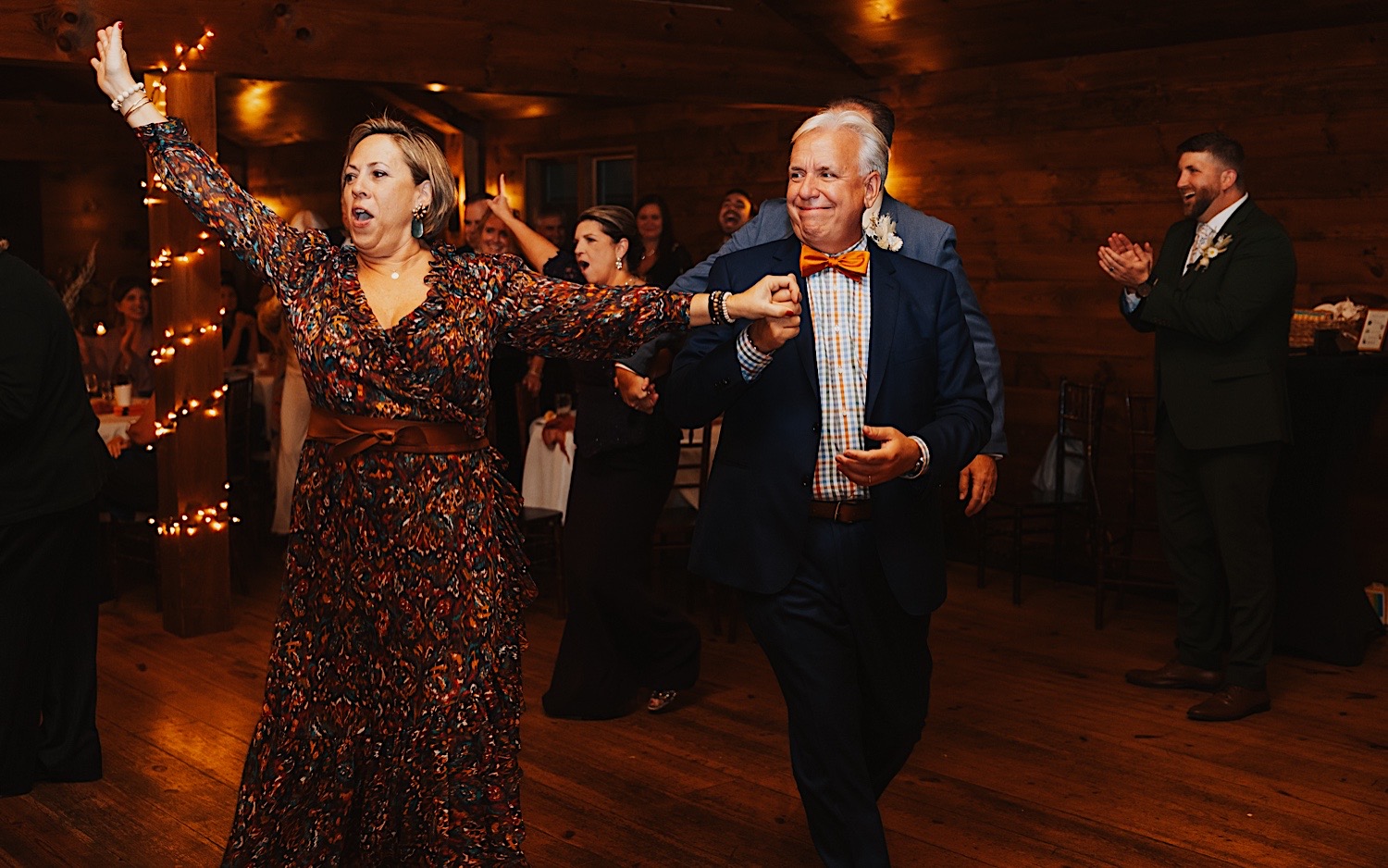 Guests of an indoor wedding reception at Lake Bomoseen Lodge in Vermont hold hands as they enter the dance floor together