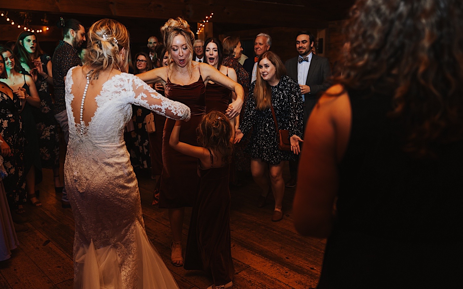 A bride dances with one of her bridesmaids and a young girl while in the middle of a dance circle during an indoor reception at Lake Bomoseen Lodge in Vermont